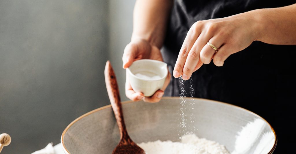 An image of a woman sprinkling a pinch of salt into a bowl of flour